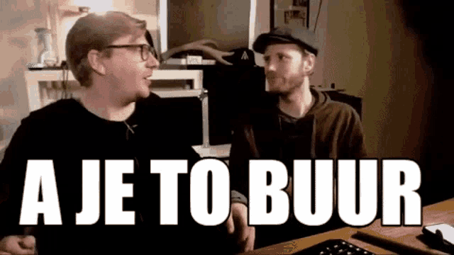 two men are sitting at a desk with the words " aje to buur " on the screen behind them