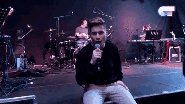 a man singing into a microphone on a stage in front of a keyboard