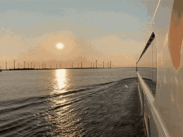 the sun is setting over a body of water with wind turbines in the background
