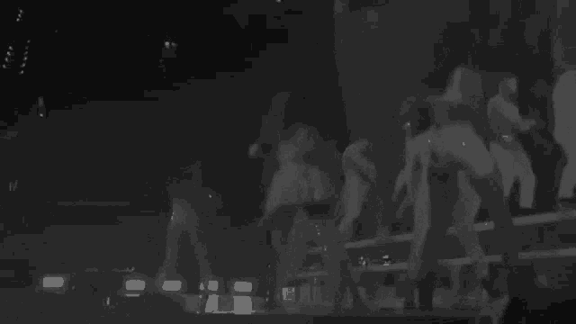 a black and white photo of a group of people dancing on a stage in a dark room .