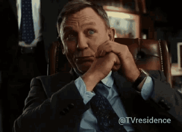 a man in a suit and tie is sitting with his hand on his chin .