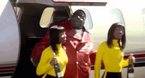 a man in a red jacket is standing next to two women in yellow sweaters holding champagne bottles .
