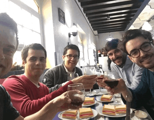 a group of men are sitting at a table toasting with wine glasses