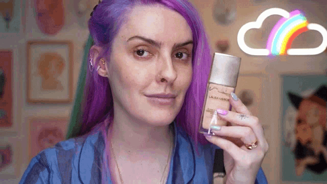 a woman with purple hair is holding a laura mercier foundation