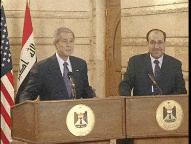 two men stand at podiums in front of flags one of which says ' islamic republic of iraq ' on it