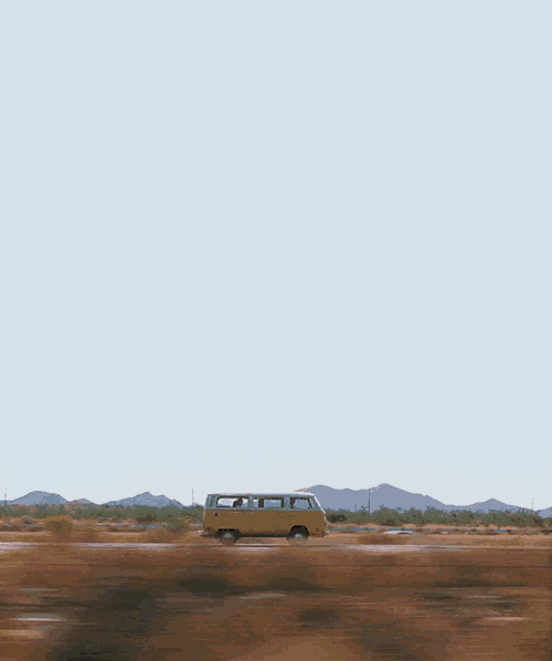 a yellow van drives down a desert road with mountains in the background