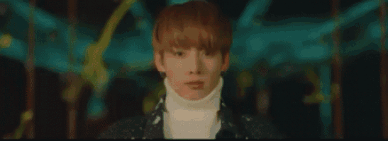 a young man wearing a white turtleneck and a black jacket is standing in front of a merry go round .
