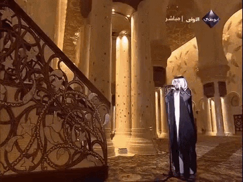 a man stands in a very ornate room with arabic writing on the corner
