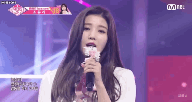 a woman is singing into a microphone while holding a flower in her mouth .