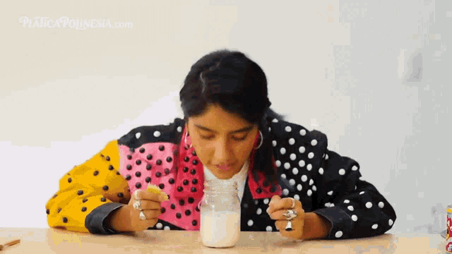 a woman in a polka dot jacket is drinking milk from a mason jar .