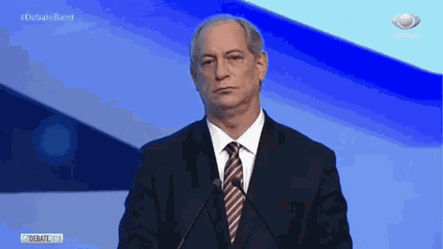 a man in a suit and tie is standing in front of two microphones .