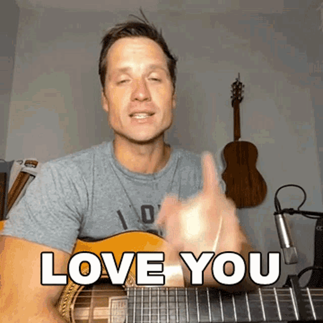 a man singing into a microphone while holding a guitar with the words love you above him