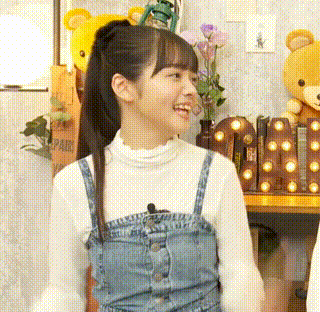 a girl in a denim dress and a white shirt is smiling in a room with stuffed animals .