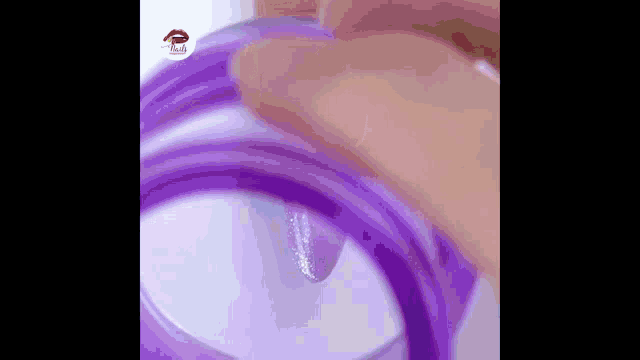 a close up of a person 's hand holding a purple bottle of liquid .