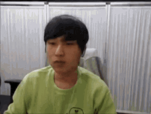 a young man wearing a green sweater is sitting in front of a white curtain .