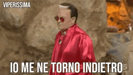 a man in a red robe and sunglasses is standing in front of a wall .