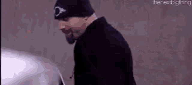 a man wearing a black beanie and a black jacket is standing in front of a car .