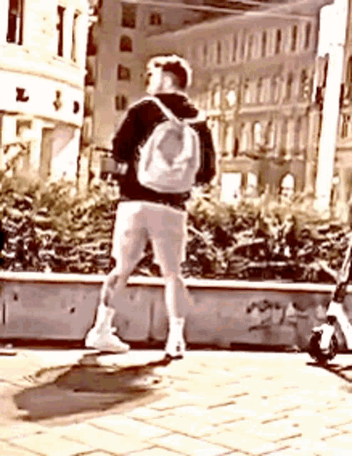 a man with a backpack is standing on a skateboard on the sidewalk