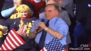 a man in a blue shirt and tie is dancing in a crowd while holding an american flag .