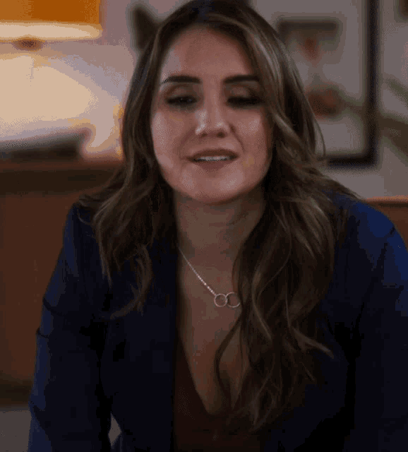 a woman wearing a blue jacket and a necklace with the letter c on it