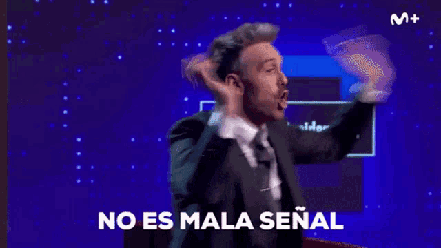 a man in a suit and tie is standing in front of a blue background and says no es mala señal .