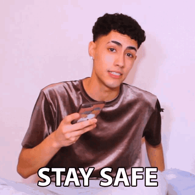 a man in a velvet shirt holds a cell phone in his hand and says stay safe