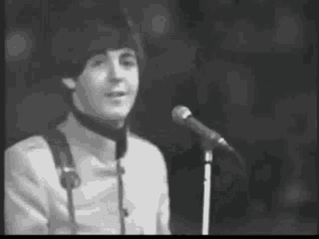 a black and white photo of a man singing into a microphone on a stage .