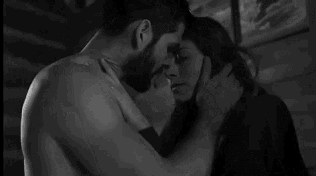 a black and white photo of a man and woman kissing in a room .