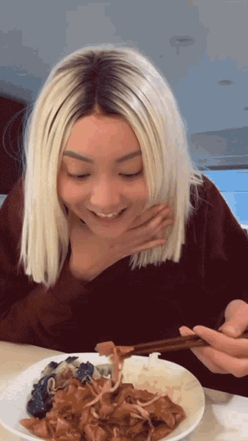 a woman with white hair is eating a plate of food with chopsticks