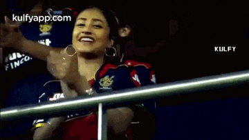 a woman is clapping her hands in the stands during a cricket game .