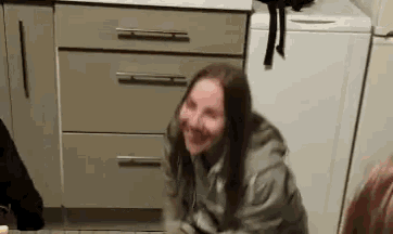 a woman is sitting on the floor in front of a washing machine and smiling .