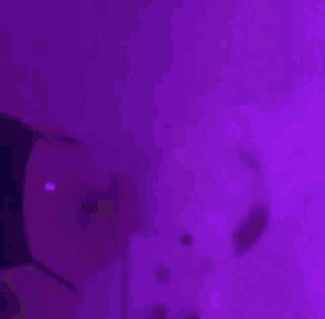 a close up of a person 's face in a dark room with purple lights .