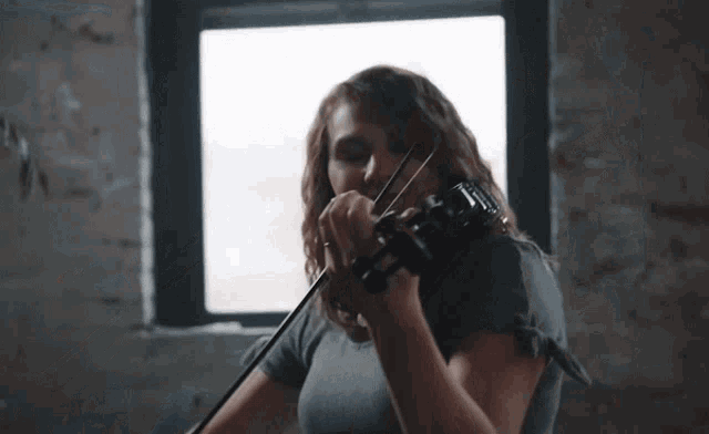 a woman in a grey shirt is playing a violin