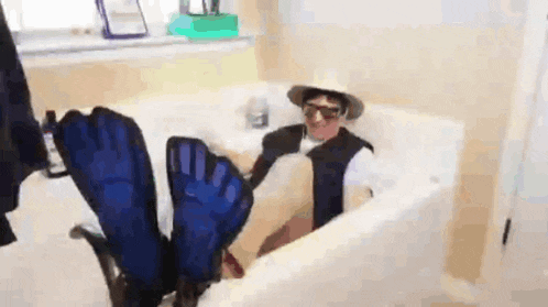 a man is sitting in a bathtub with his feet up and a hat on .