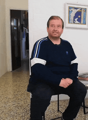 a man wearing a blue adidas sweater sits on a chair