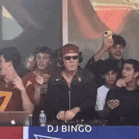 a group of young men are sitting in a stadium watching a dj playing music .