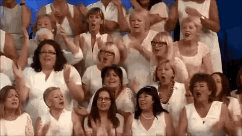 a large group of women are singing in a choir and clapping their hands .