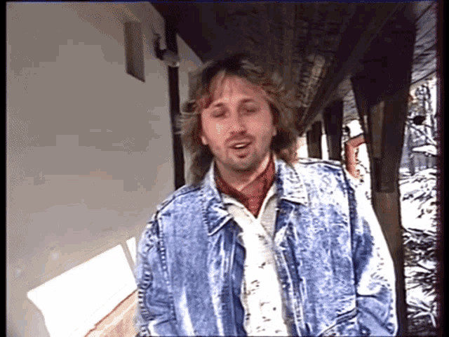 a man wearing a blue denim jacket and a red scarf stands in a hallway