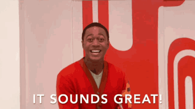 a man in a red sweater says it sounds great in front of a red wall