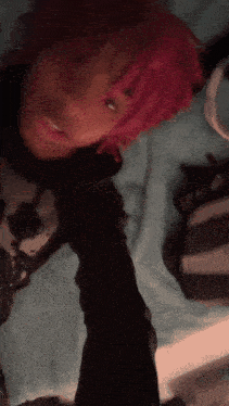 a person with pink hair is laying on a bed and taking a selfie .