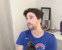 a man wearing a blue cubs shirt is sitting in front of a microphone in a room .