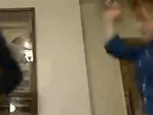 a person in a blue shirt is standing in front of a door and holding a remote control .