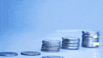 a stack of coins sits in front of a computer screen showing a financial graph