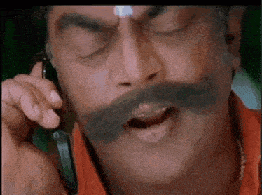 a man with a big mustache is talking on a cell phone .