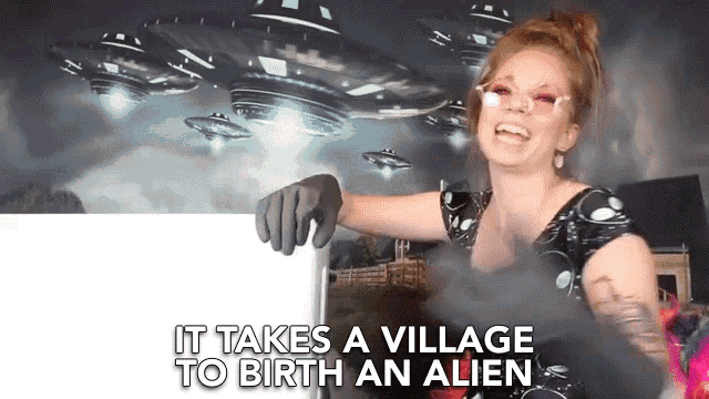 a woman is pointing to a sign that says it takes a village to birth an alien