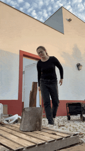 a woman standing on a wooden pallet next to a stump