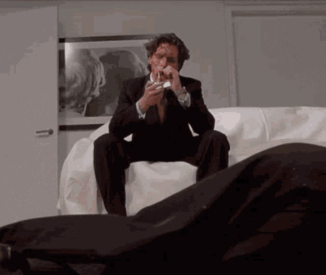 a man in a suit is sitting on a couch smoking a cigarette