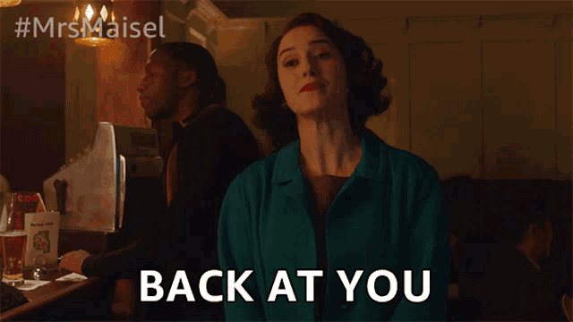 a woman in a green jacket is standing in front of a sign that says " back at you "
