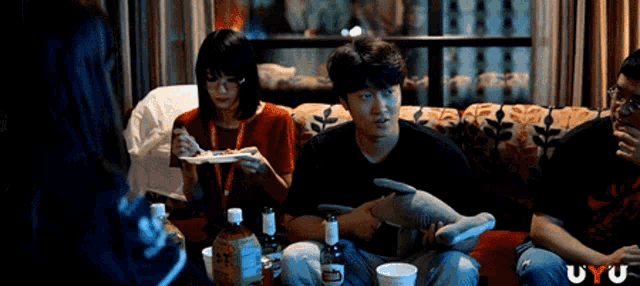 a group of people are sitting on a couch eating and drinking with the word uyu on the bottom right