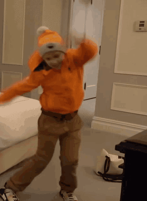 a young boy wearing an orange jacket and a white hat is dancing